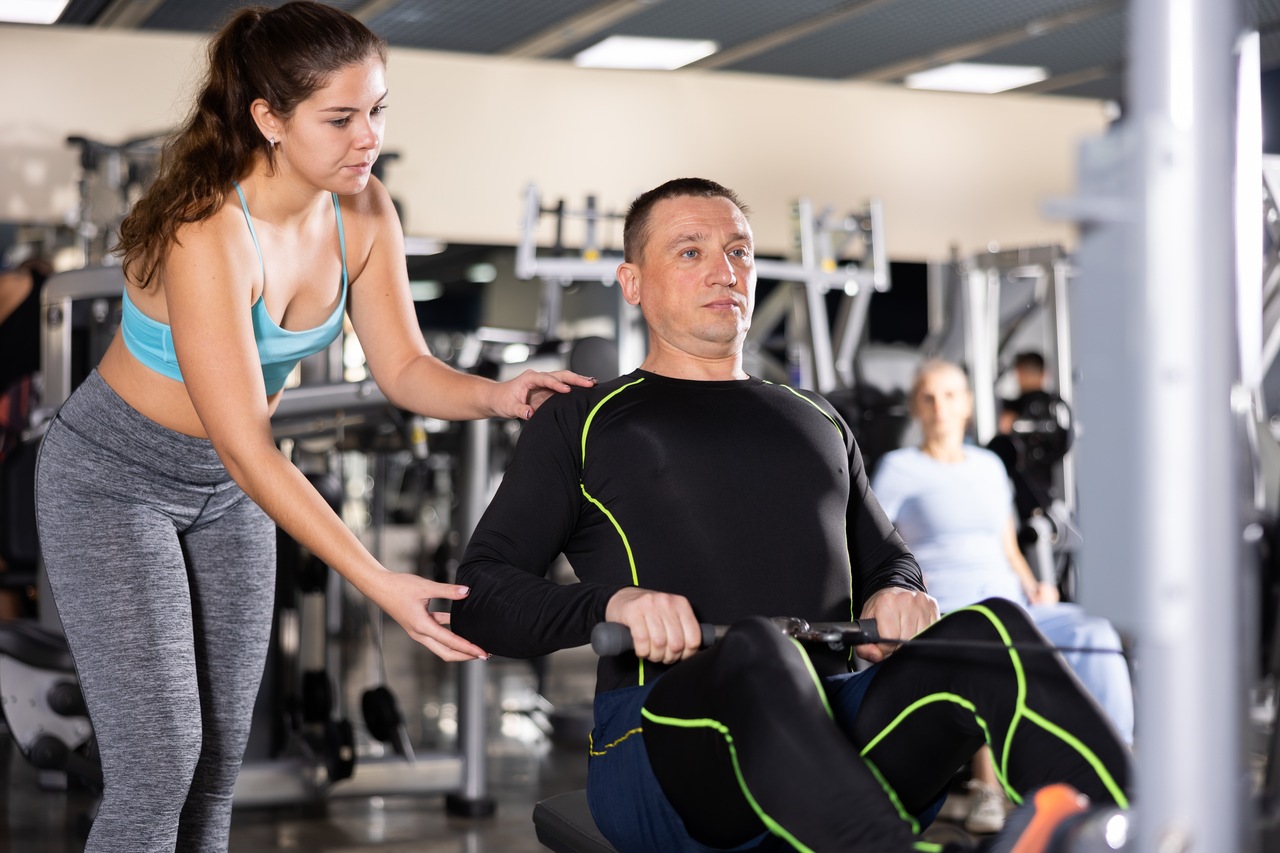homem fazendo exercício na academia auxiliado por uma instrutora