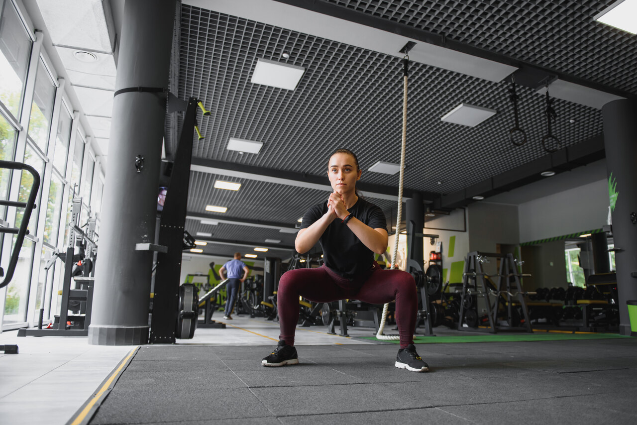 mulher fazendo o exercício agachamento sumô na academia